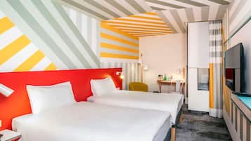 A hotel room with two beds, a desk, a chair, a TV, and a striped ceiling.