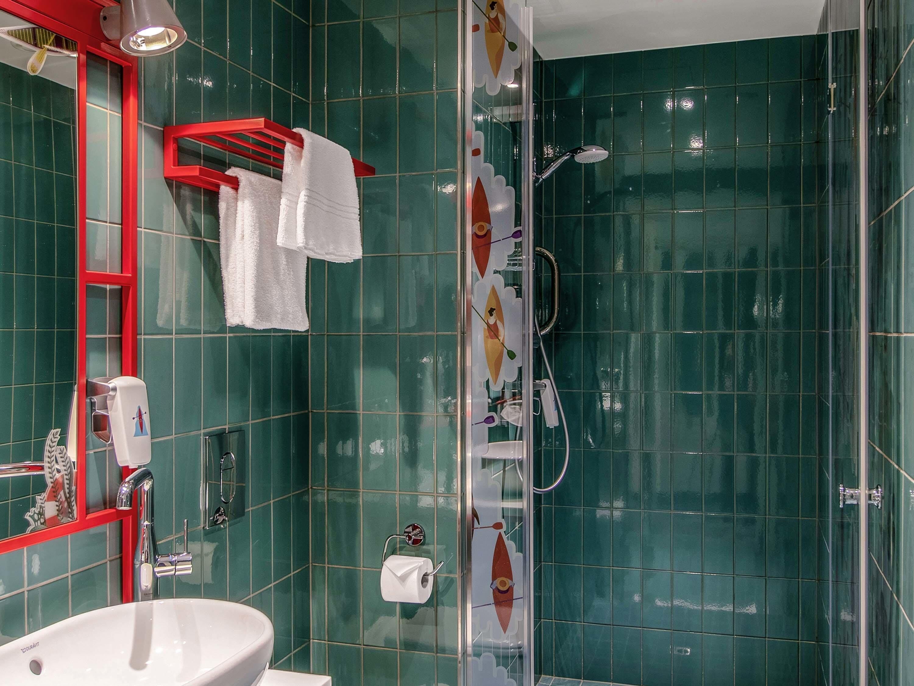 A bathroom with green tiles, a white sink, a red towel rack, and a shower with a glass door.
