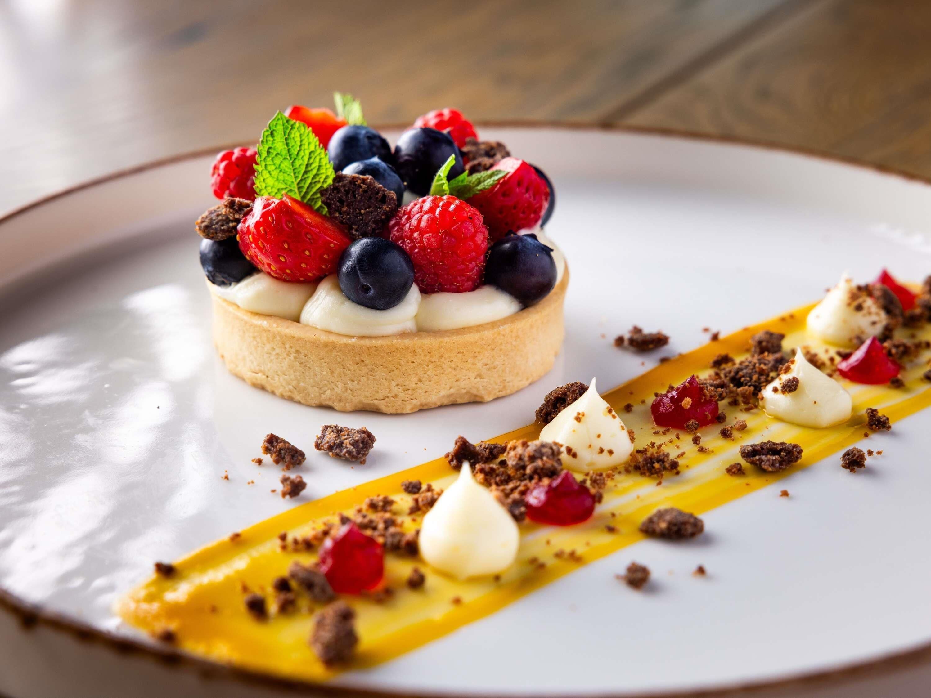A dessert with a tart base, topped with strawberries, blueberries, and mint leaves.