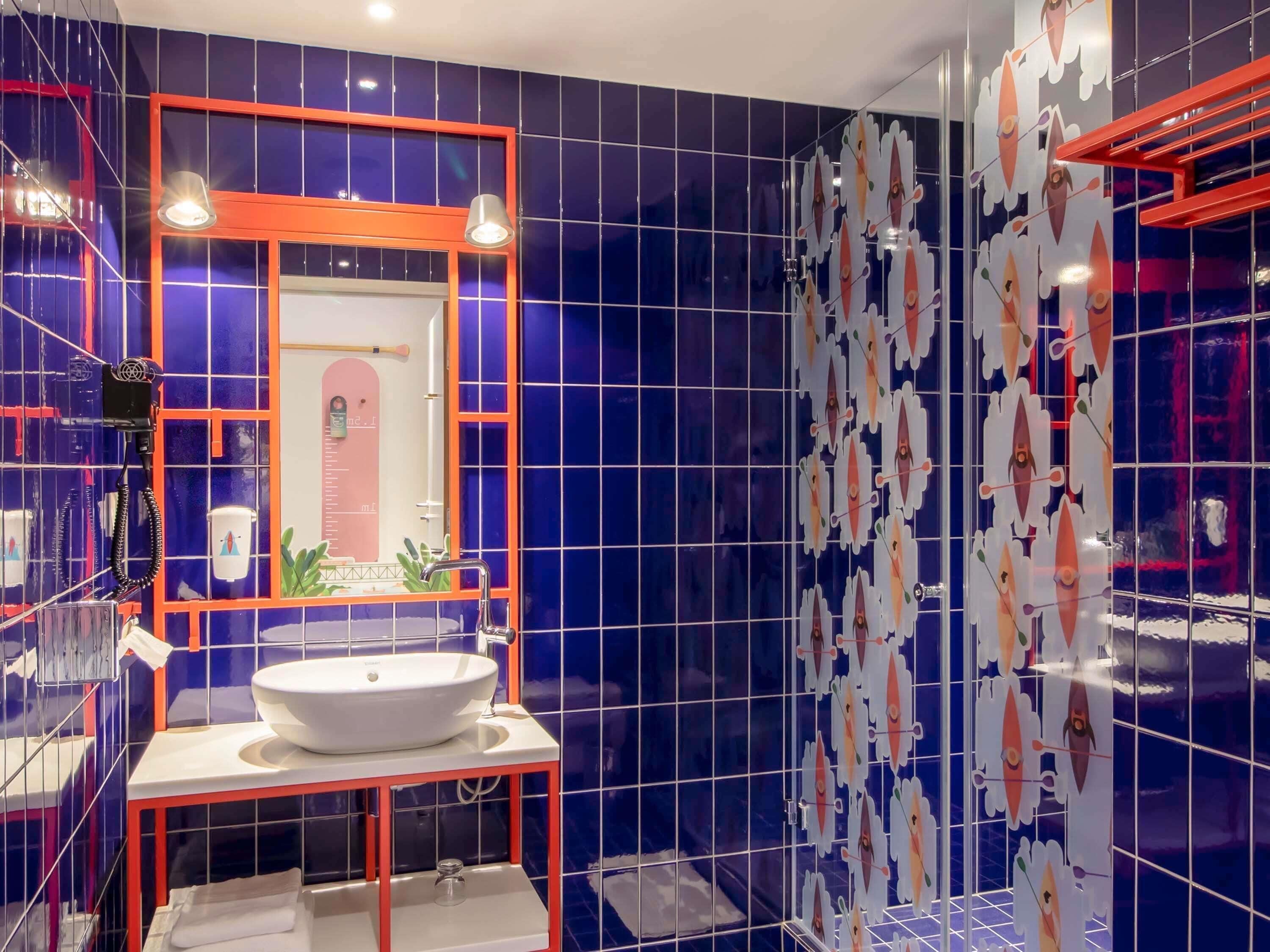 Un bagno con un lavandino bianco, uno specchio dalla cornice arancione e pareti rivestite di piastrelle blu.