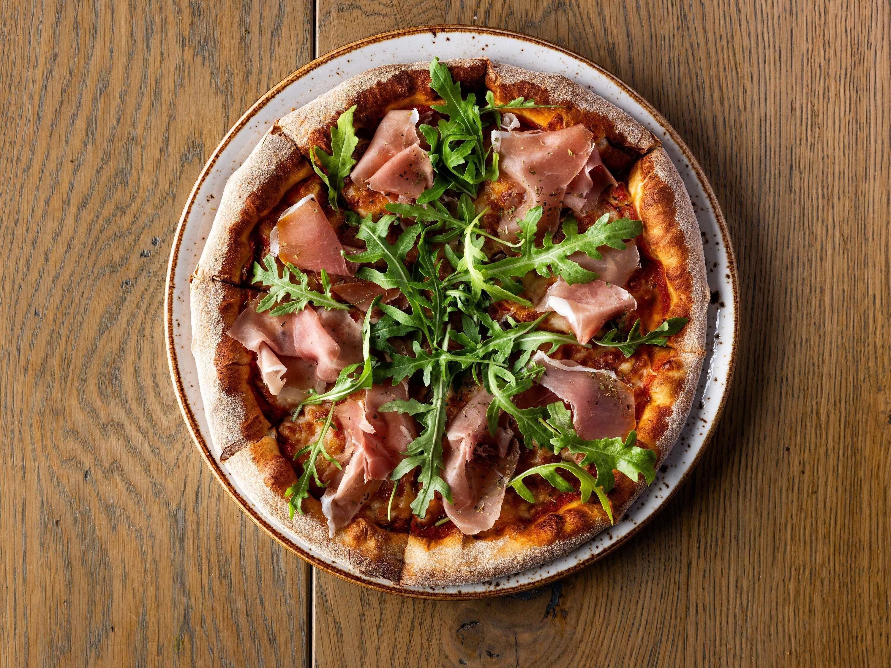 Une pizza à la jambon de Parme et à la roquette, servie sur une assiette ronde.