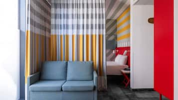 Une chambre moderne avec un canapé bleu, un lit doté d’une tête de lit rouge et un rideau à rayures.