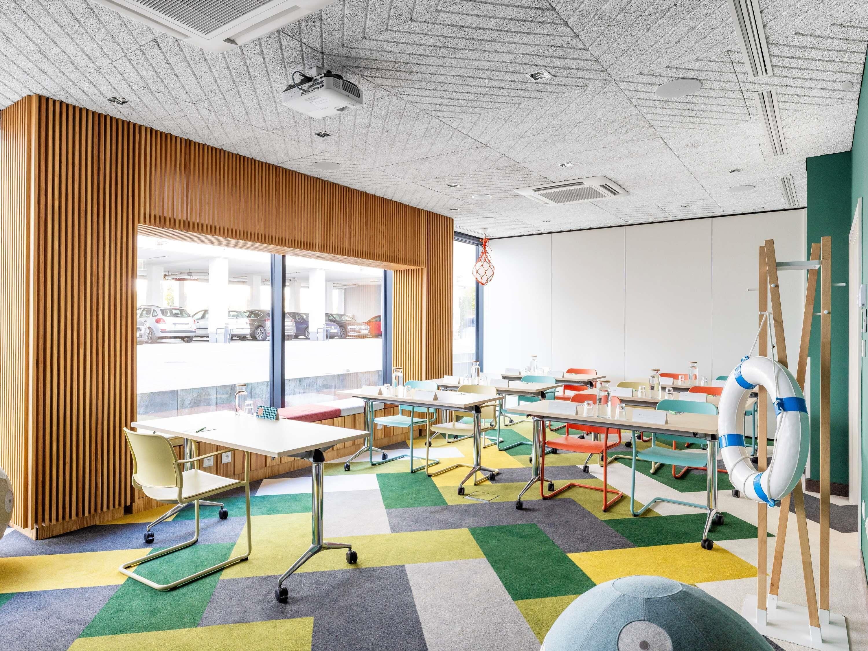 A classroom with tables, chairs, a projector, and a view of parked cars outside.