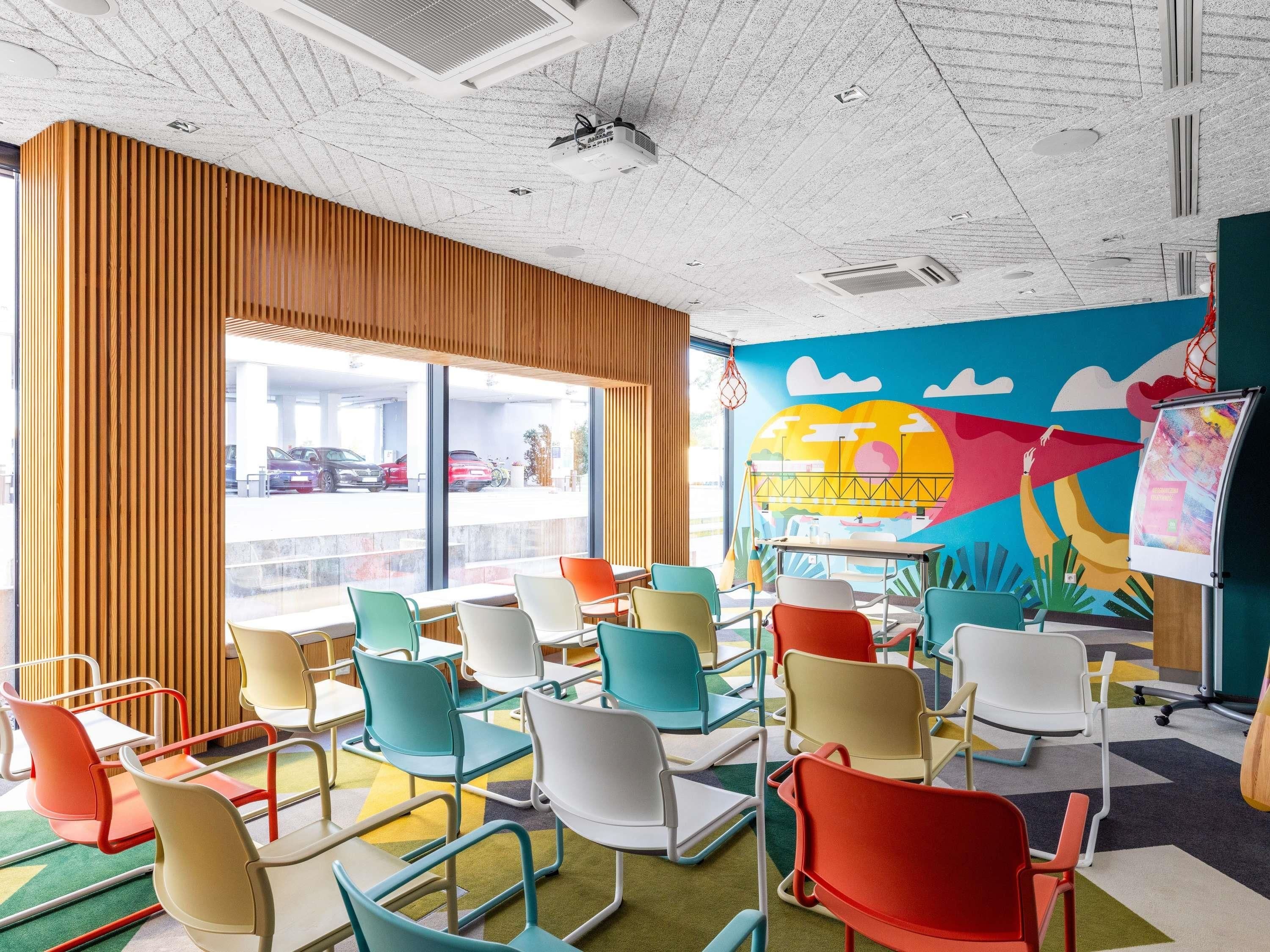 A brightly colored room with a large window, colorful chairs, and a mural on the wall.