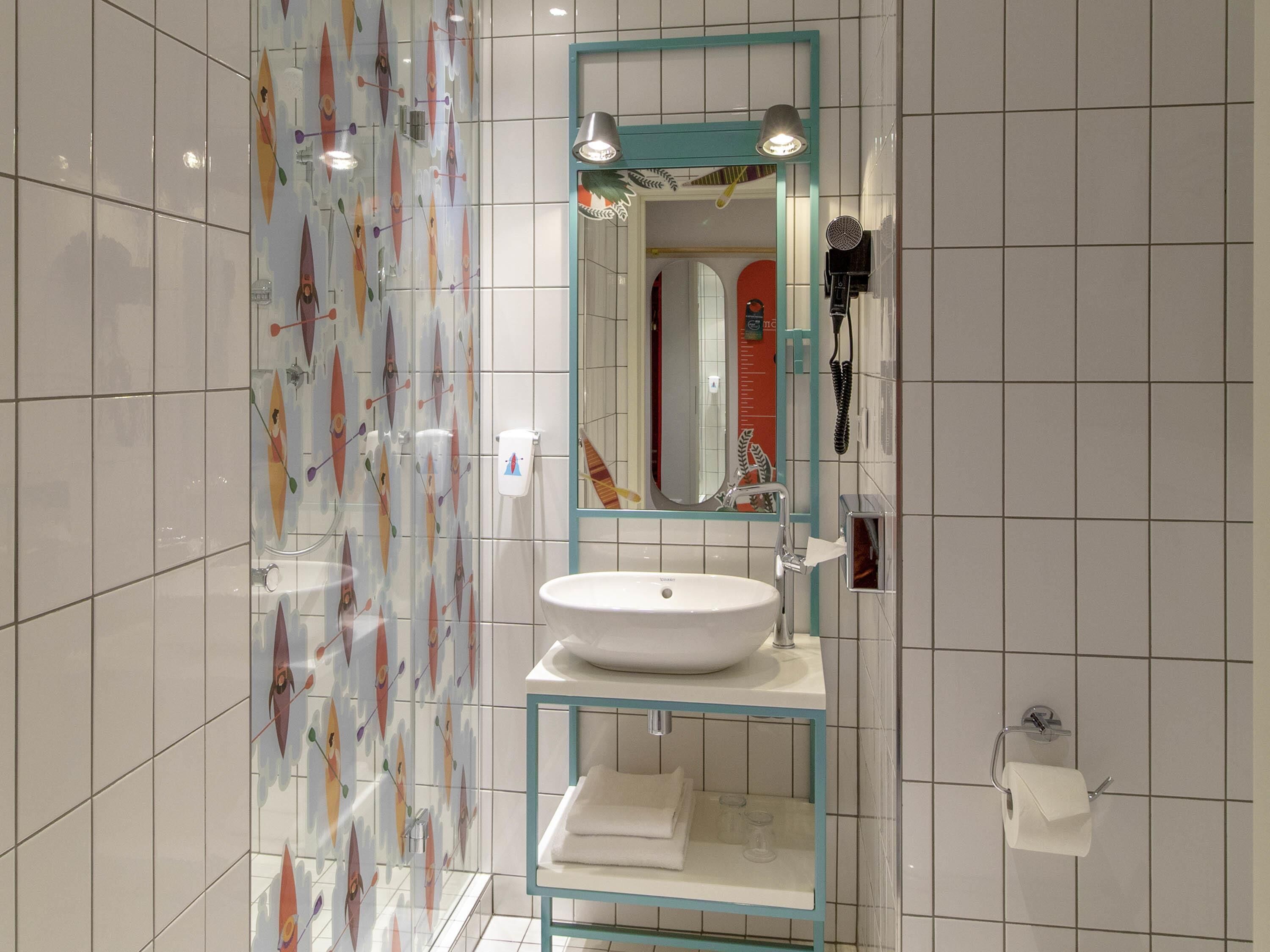 Une salle de bain moderne avec un lavabo blanc, une cabine de douche en verre et un miroir doté d’un cadre de couleur turquoise.
