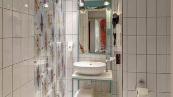 Un baño moderno con un lavabo blanco, cabina de ducha con paredes de vidrio y espejo con marco verde azulado.