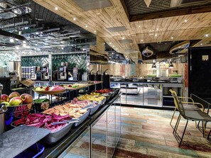 A buffet area with various food options, a kitchen in the background, and a wooden ceiling. - ibis Styles Warszawa Centrum (Warsaw)