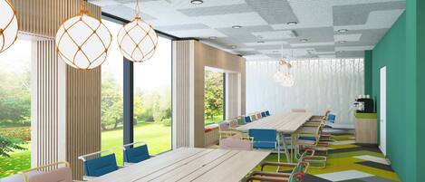 A modern meeting room with a long table, colorful chairs, and large windows offering a view of a garden.
