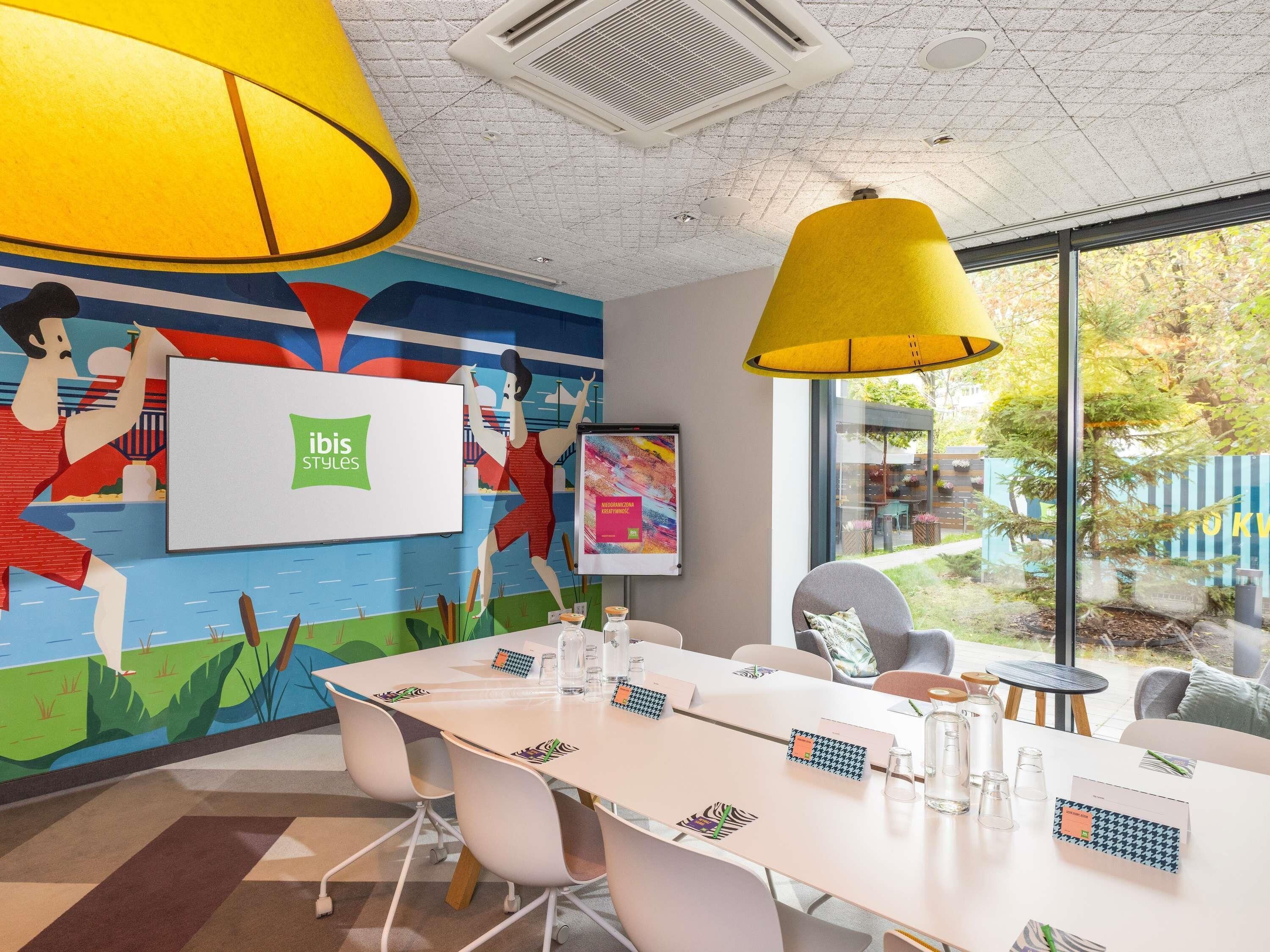 A modern meeting room with a large table, colorful wall art, and large yellow pendant lights.