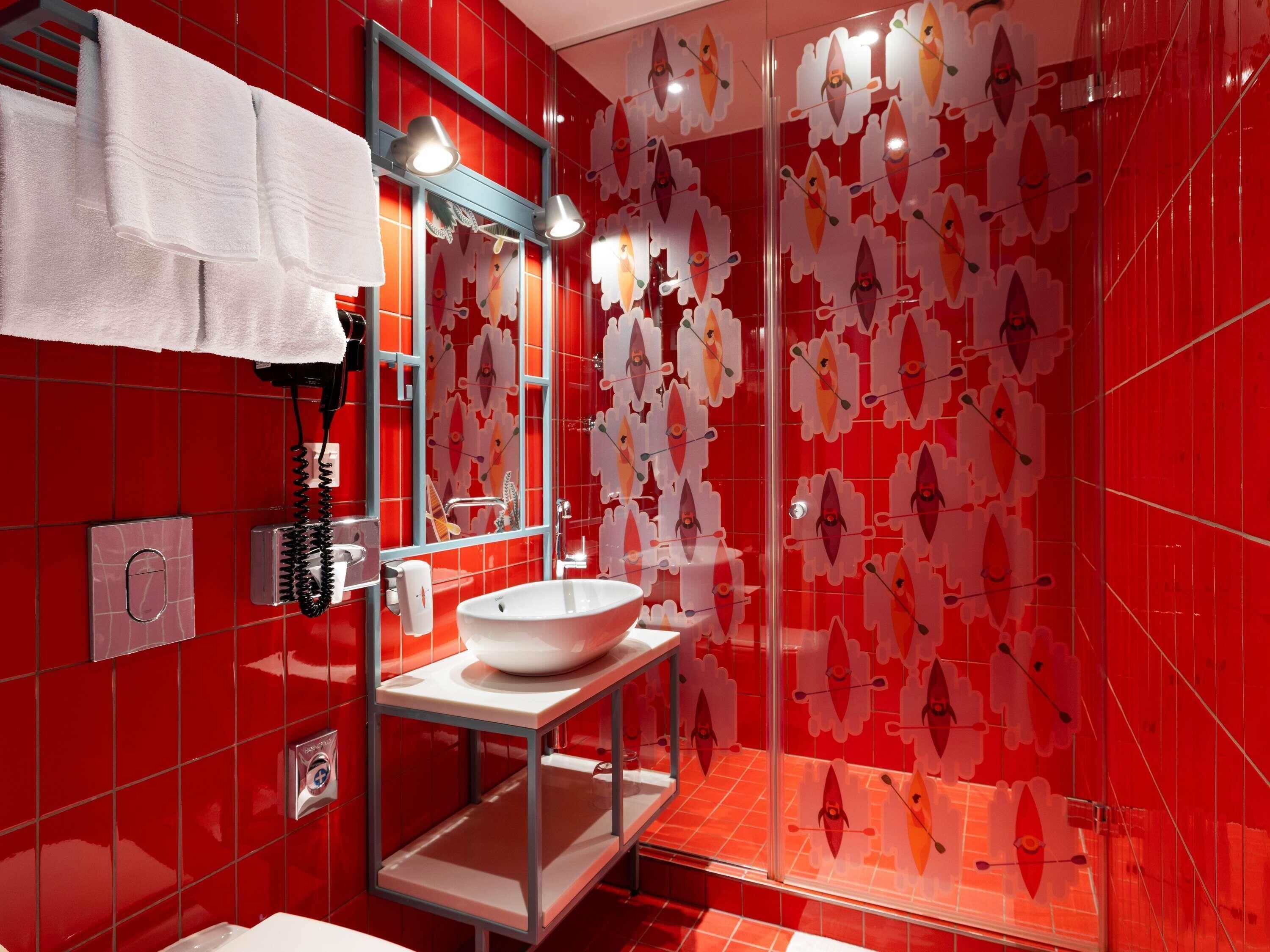 Ein modernes Badezimmer mit roten Fliesen, einem weißen Waschbecken und einer Glasdusche.