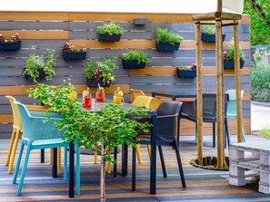 An outdoor seating area with a wooden wall and hanging planters, featuring a variety of plants and a table with chairs. - ibis Styles Warszawa Centrum (Warsaw)