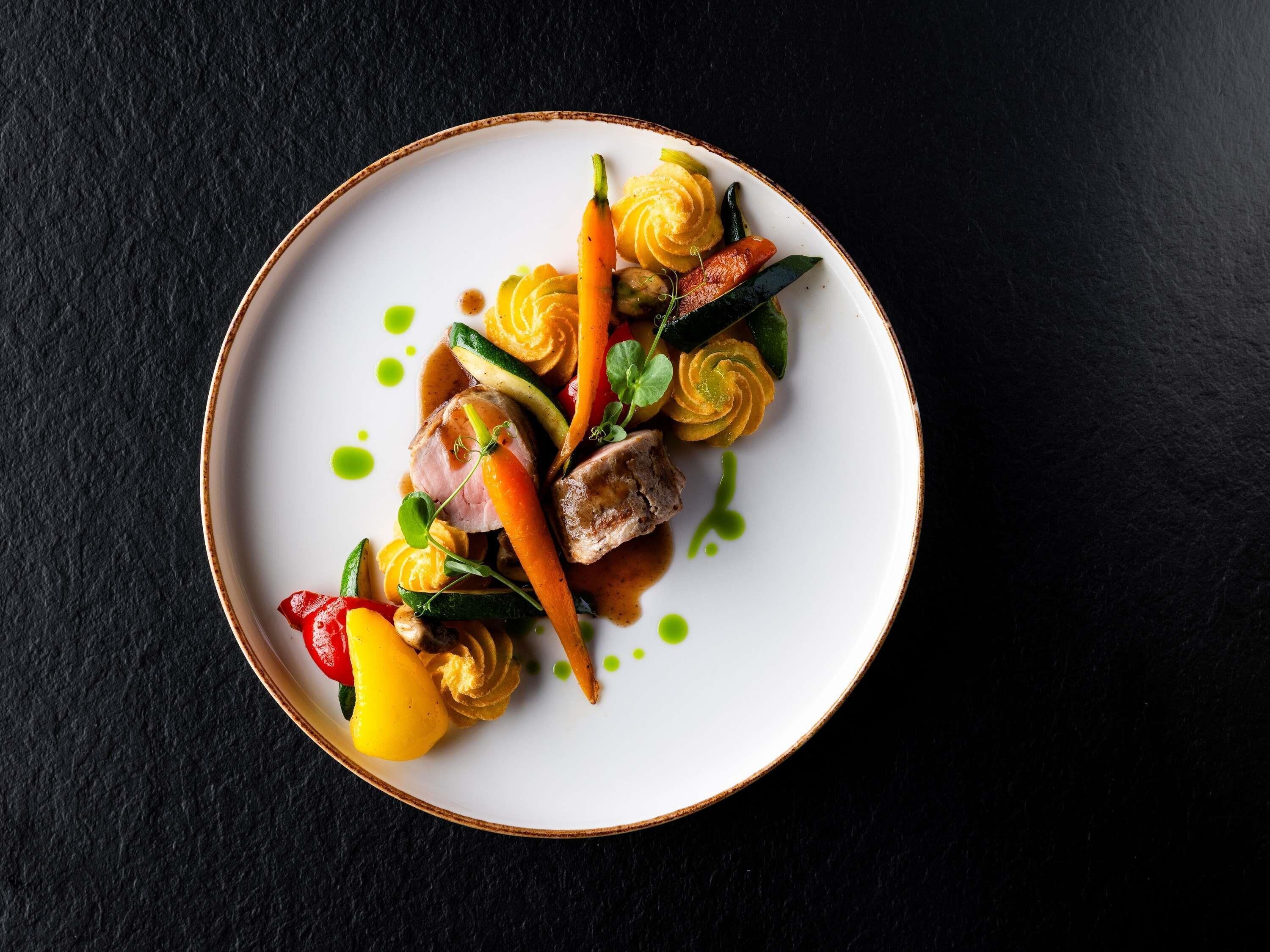 A plate of food with various vegetables and a piece of meat, served on a white plate with a brown rim.