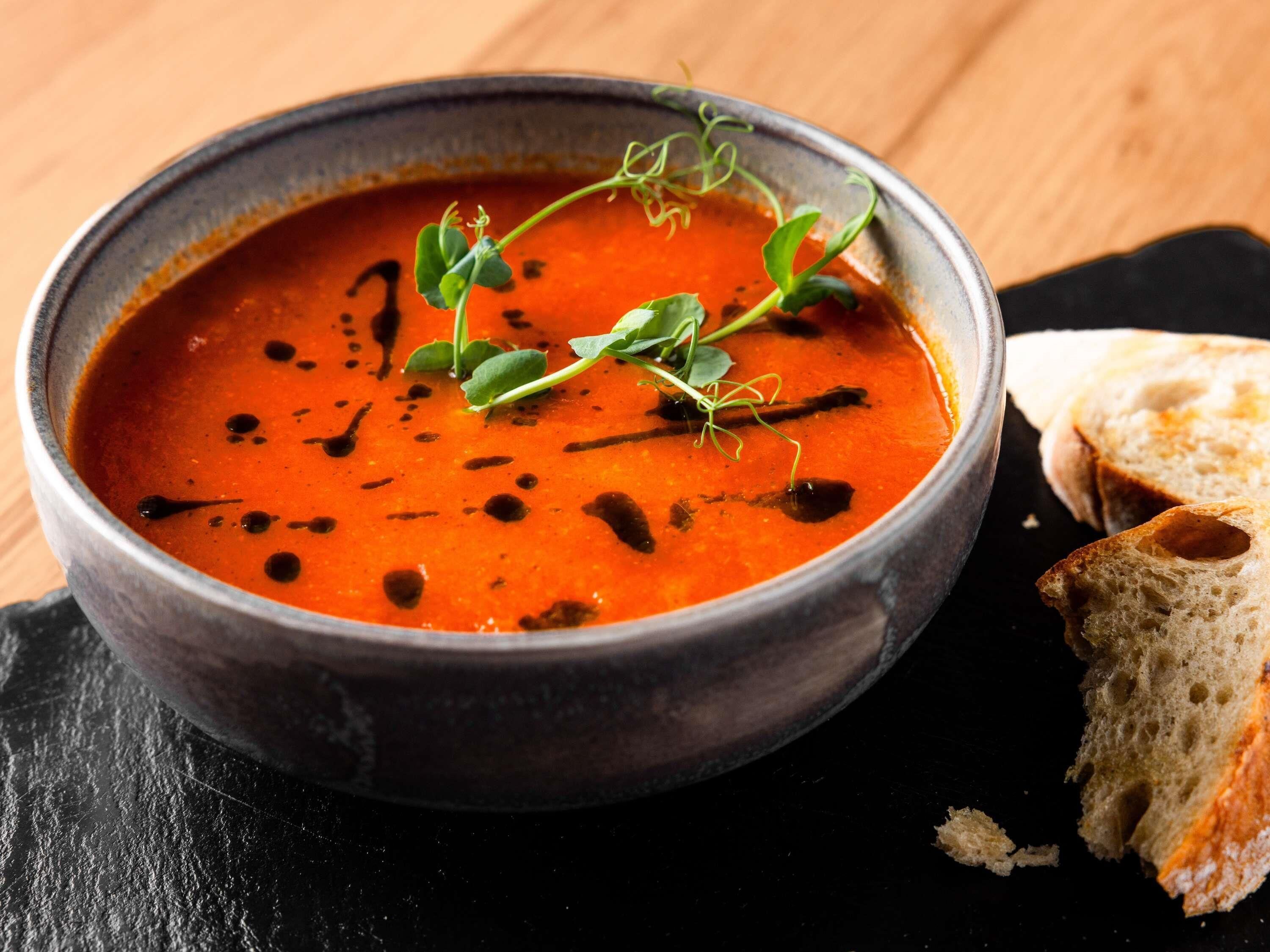 A bowl of soup garnished with herbs, accompanied by slices of bread on a dark surface.