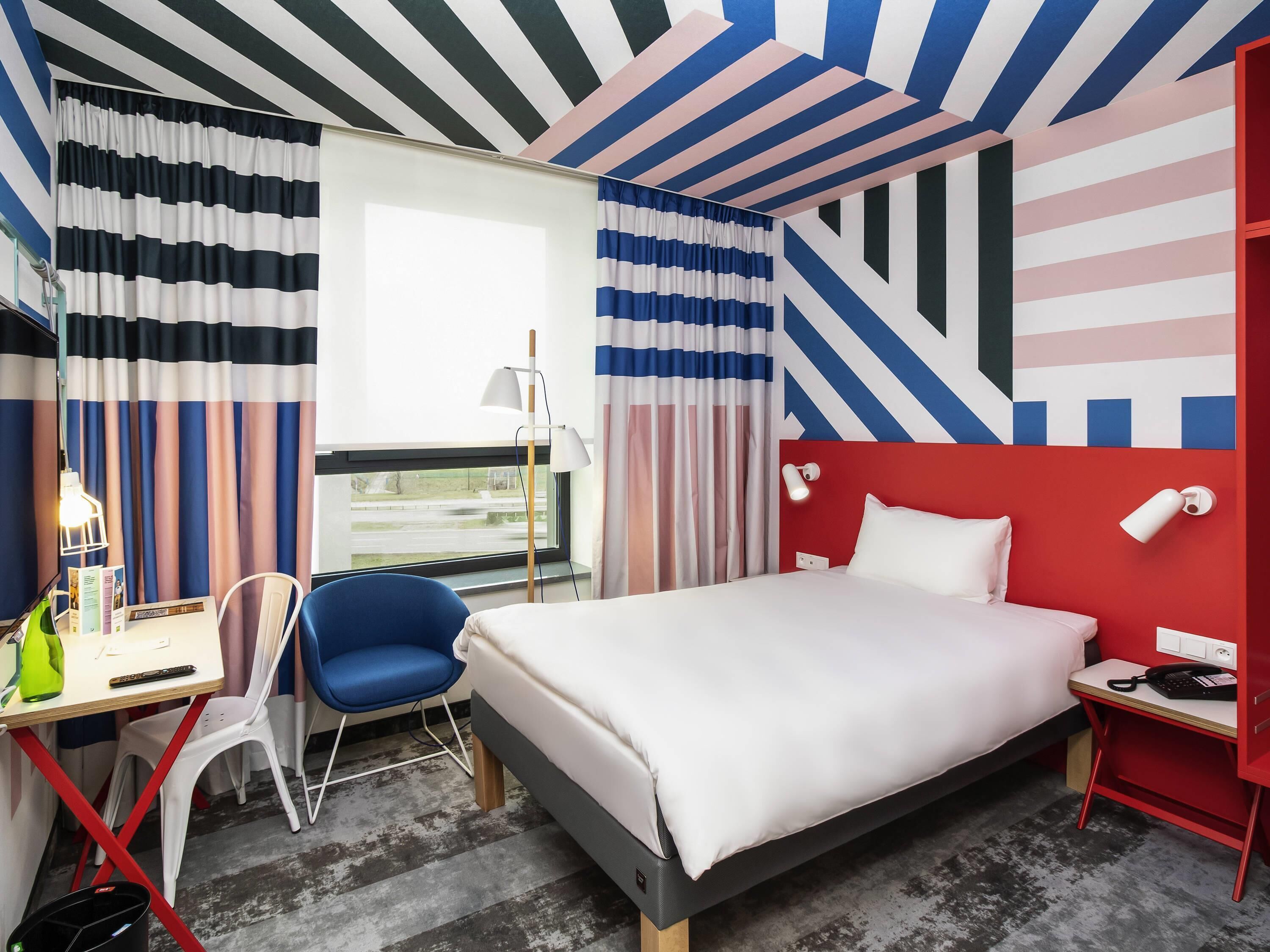 A hotel room with a bed, desk, chair, and a view of the outside.