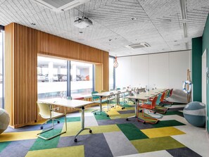 A conference room with a large table, colorful chairs, a projector, and a view of parked cars outside. - ibis Styles Warszawa Centrum (Warsaw)