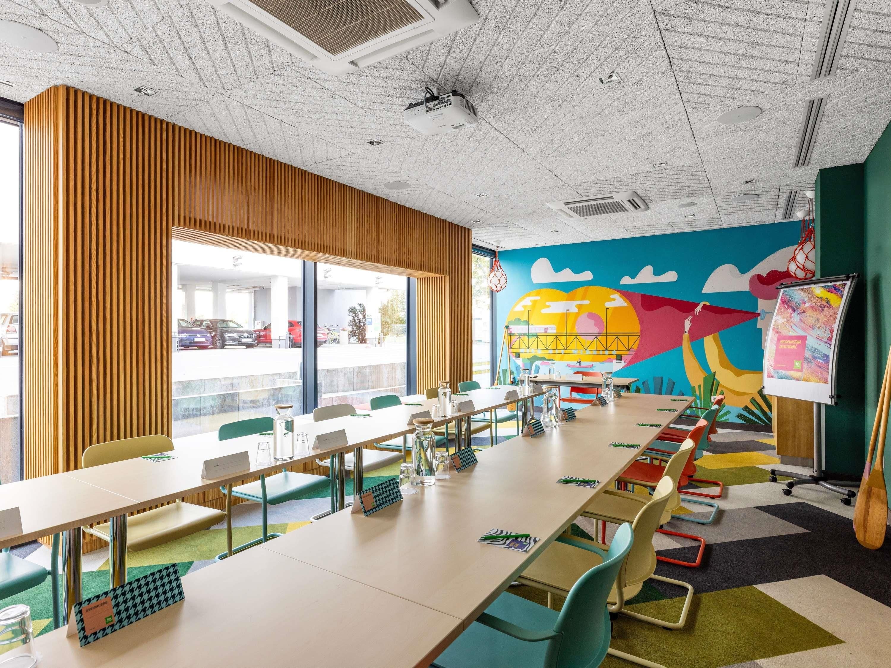 Un salón de conferencias con una larga mesa, sillas y un mural colorido en la pared.
