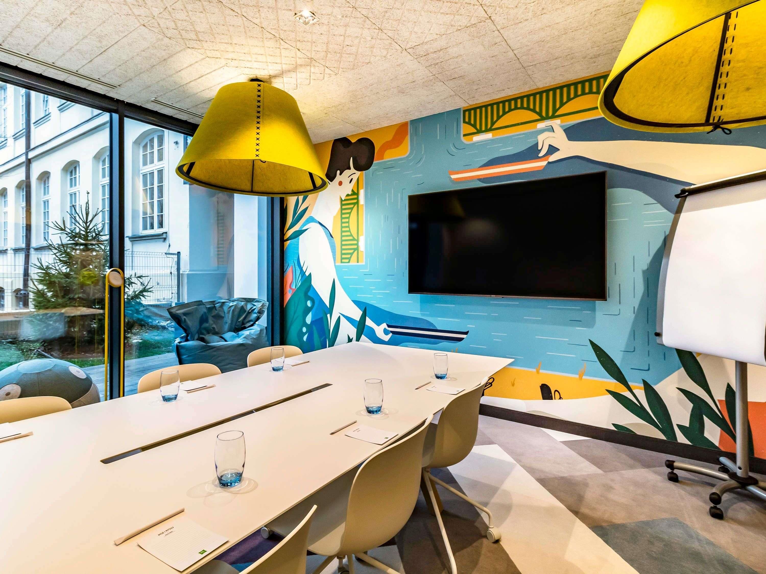 Een moderne vergaderruimte met een grote tafel, stoelen, een televisie en een muurschildering.