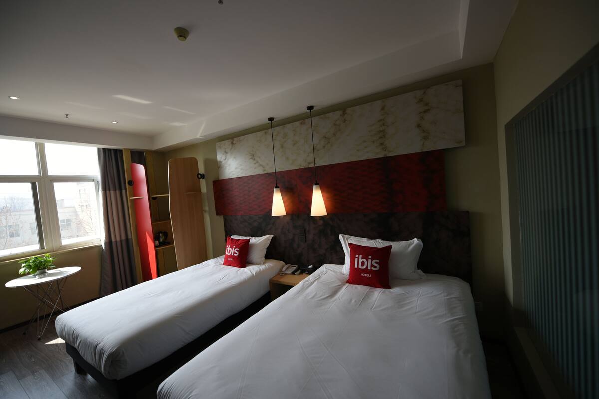 Een hotelkamer met twee bedden, een tafeltje met een plant en een raam met gordijnen.