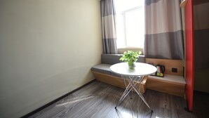 Een kleine kamer met een raam, een ronde tafel met een plant, een bank en een rode deur.