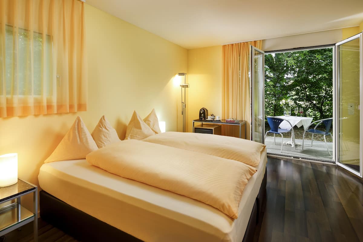 Une chambre d’hôtel avec un grand lit, un bureau avec une lampe et une vue sur l’extérieur grâce à une porte vitrée.