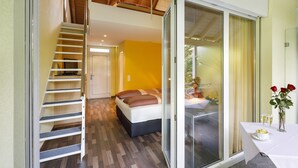 Habitación de hotel moderna con una escalera de madera, una cama con cabecera oscura y un rincón comedor con mesa para dos.
