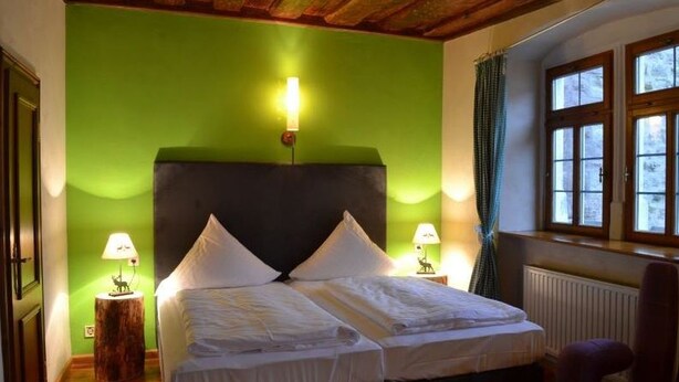 A room with a bed, two bedside lamps, a window with curtains, and a radiator. - Hotel Turmdieb (Volkach)