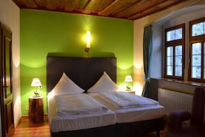 Una stanza con un letto, due abat-jour, una finestra con tende e un termosifone.