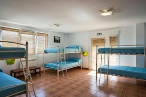A dormitory room with bunk beds, a small table, and a window with blinds.