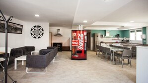 Una sala de estar moderna con dardos, una máquina expendedora de Coca-Cola y una zona de cocina con comedor.