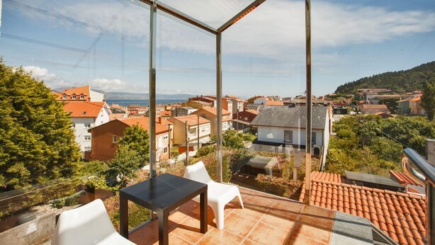 Un balcón acristalado con vistas a un pueblo, una mesa y dos sillas.