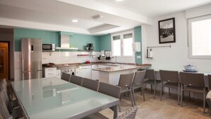 Cocina moderna con comedor, que incluye una isla grande, muebles blancos y una pared de acento color turquesa.
