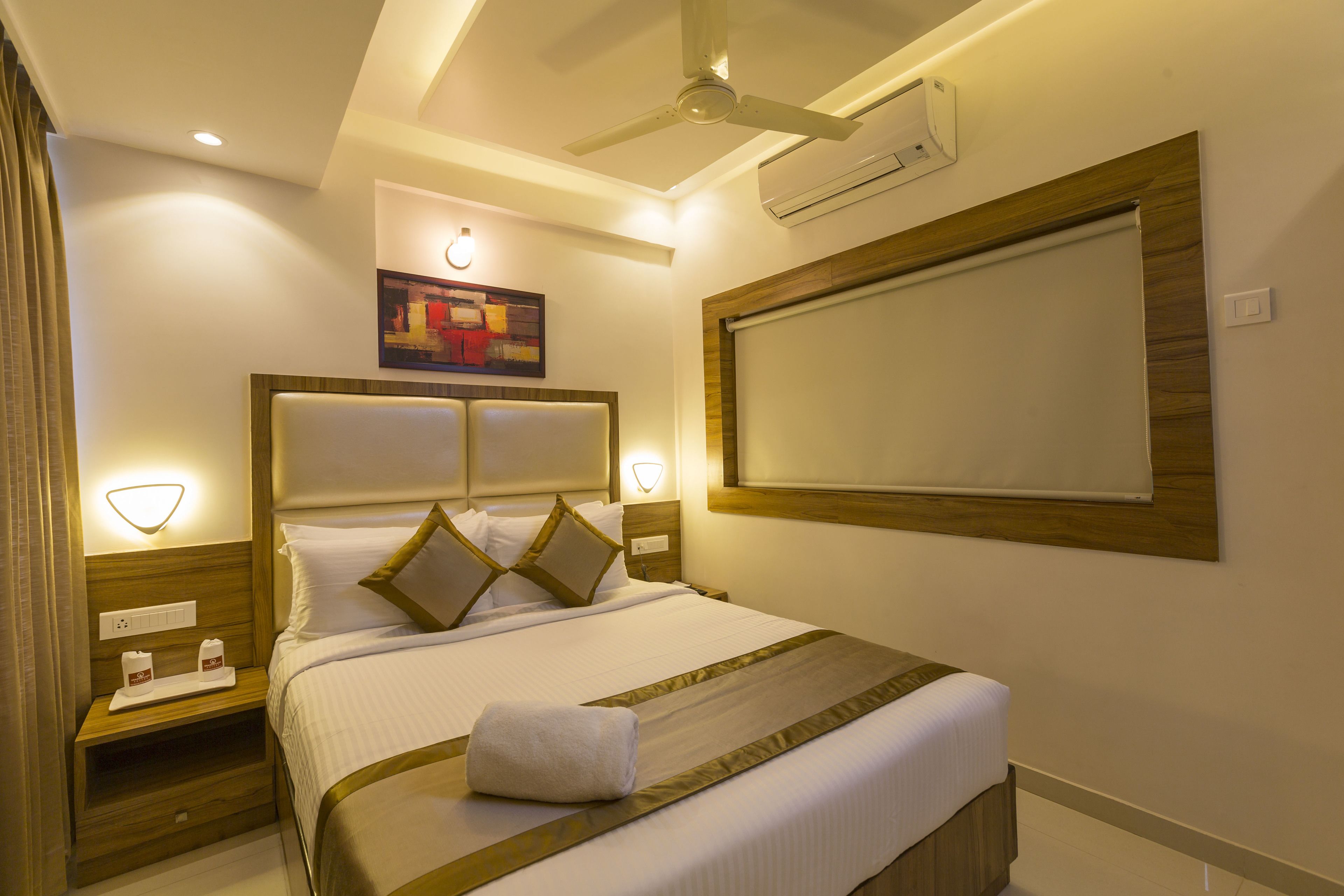 Habitación de hotel bien iluminada con una cama grande, un ventilador de techo y aire acondicionado de pared.
