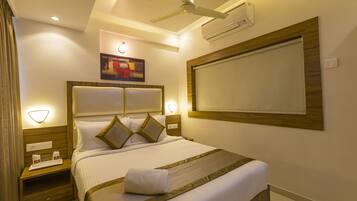 Habitación de hotel bien iluminada con una cama grande, un ventilador de techo y aire acondicionado de pared.