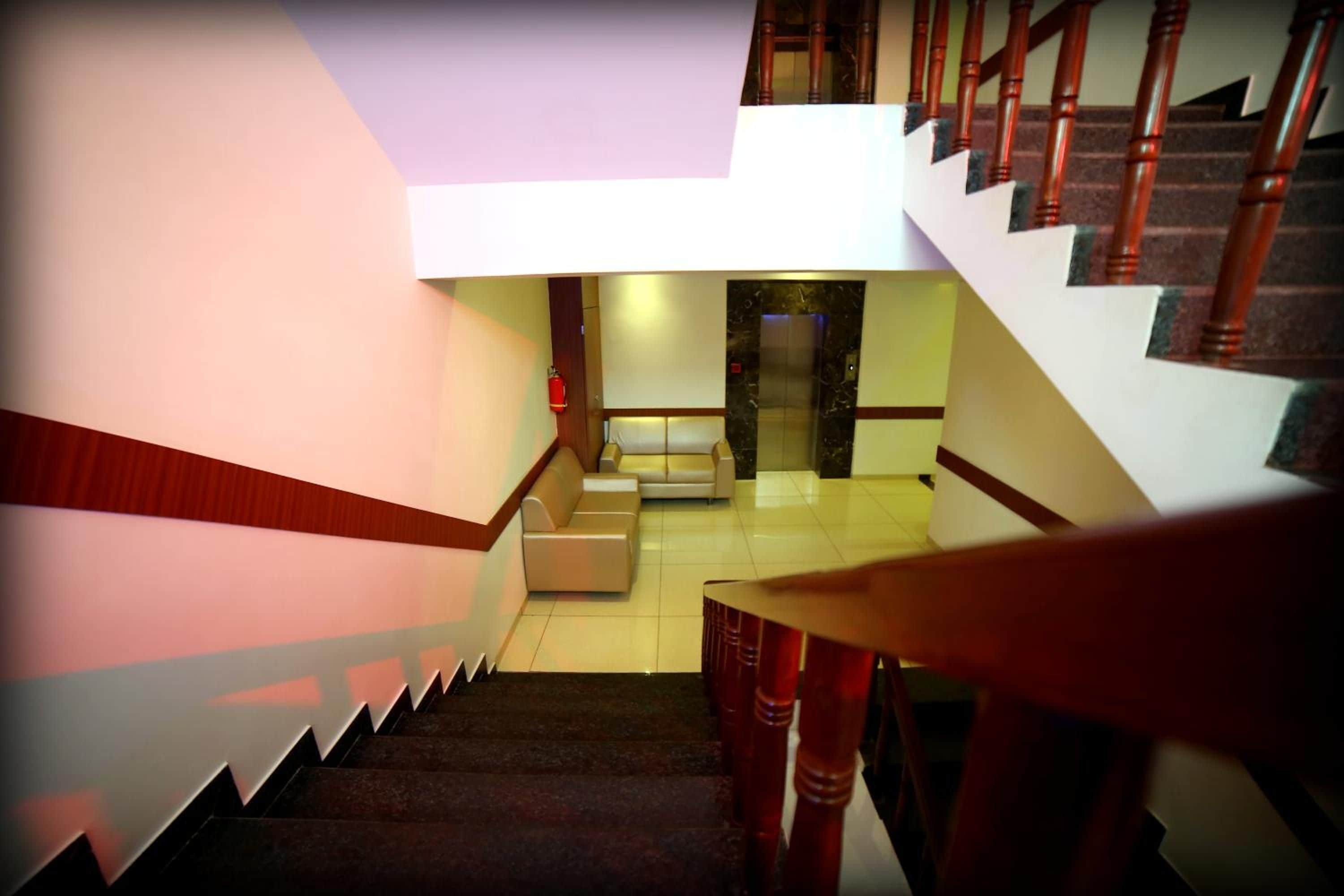 Eine Treppe mit hölzernen Geländern führt zu einer Zwischenebene mit einem Sofa und einem Feuerlöscher.