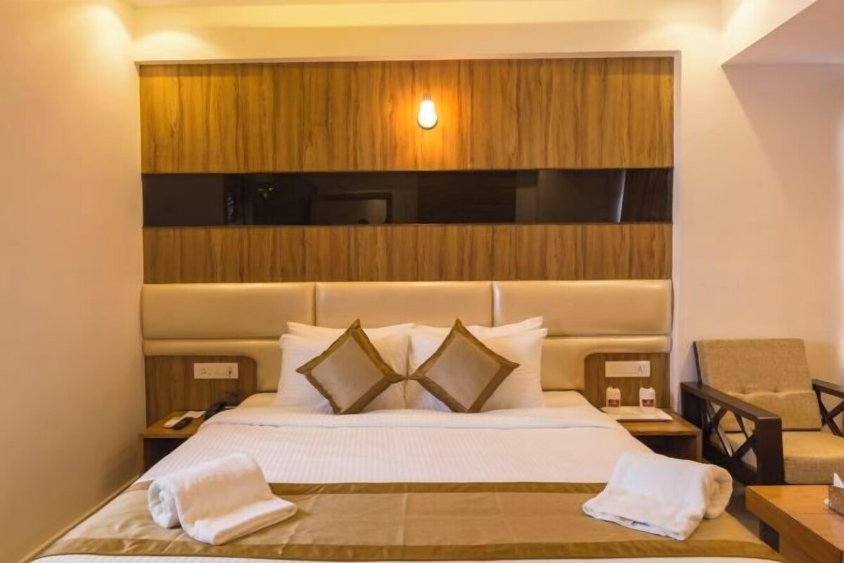 A hotel room with a large bed, a wooden headboard, a nightstand, and a chair.