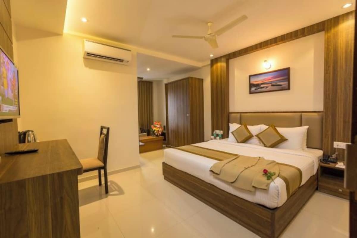 A hotel room with a large bed, a desk, and a chair. There is a ceiling fan and an air conditioning unit.