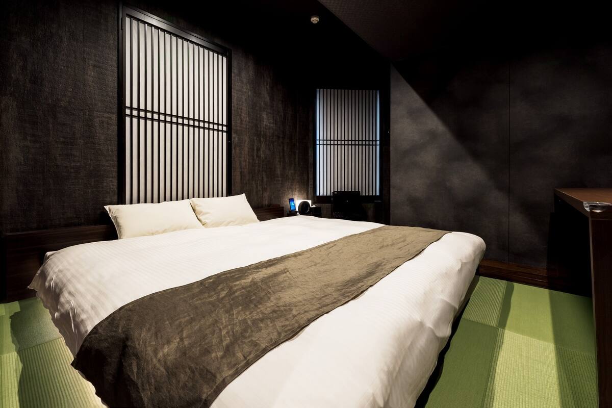 Una habitación de hotel moderna con una cama grande, paredes oscuras y ventanas amplias.
