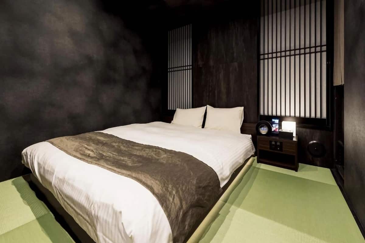 Una habitación con cama, mesita de noche y un altavoz.