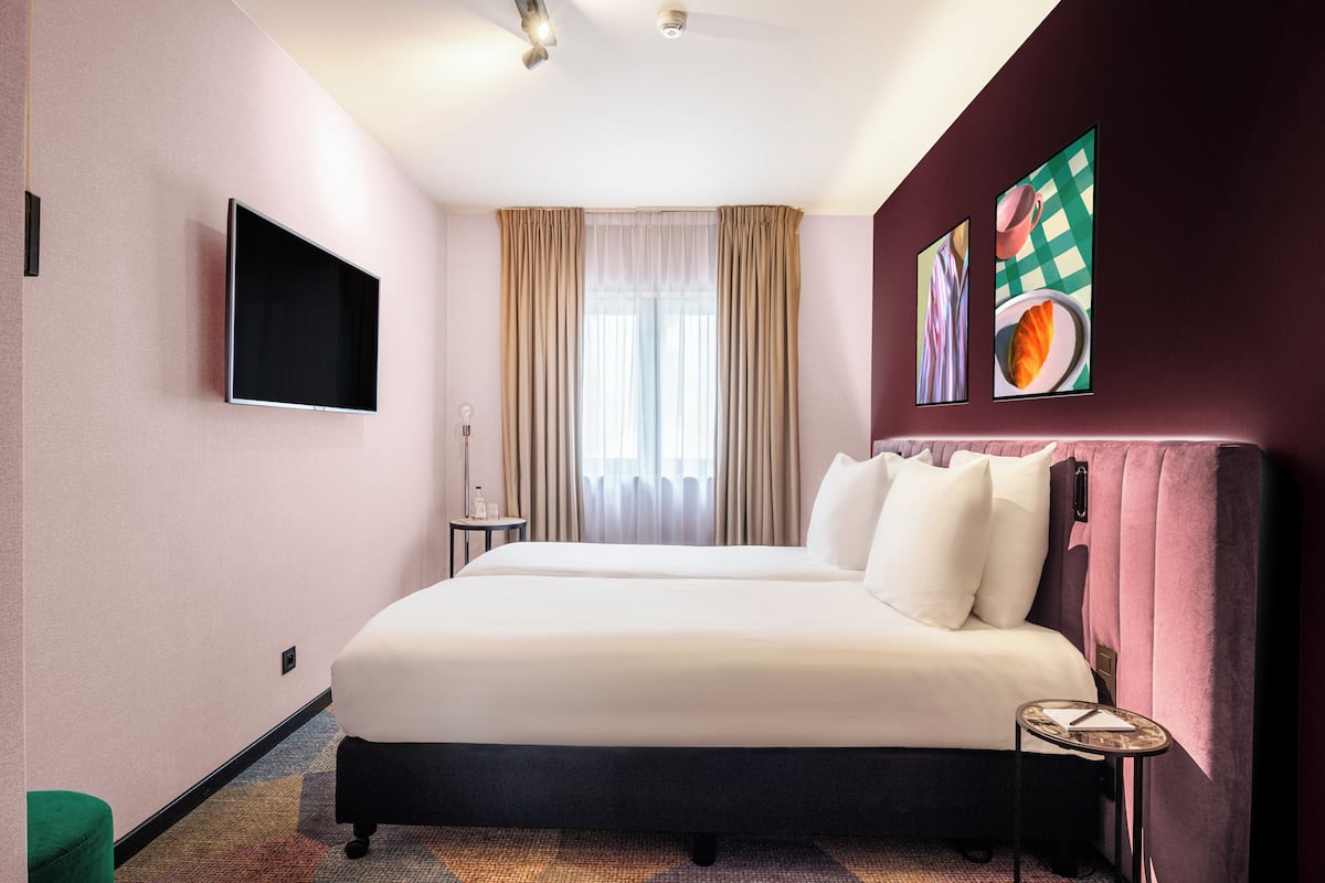 Habitación de hotel con una cama grande, un televisor de pantalla plana, una ventana con cortinas y obras de arte en la pared.