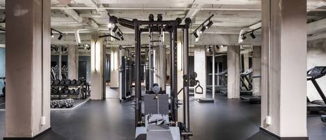 Un gimnasio con equipo de ejercicio, cintas de correr y racks para pesas.