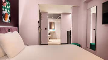 Habitación de hotel con cama, una silla verde, un espejo y vistas al baño y la cocina.