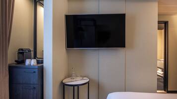 A hotel room with a bed, a TV mounted on the wall, a small table with a coffee maker and glasses, and a wardrobe.
