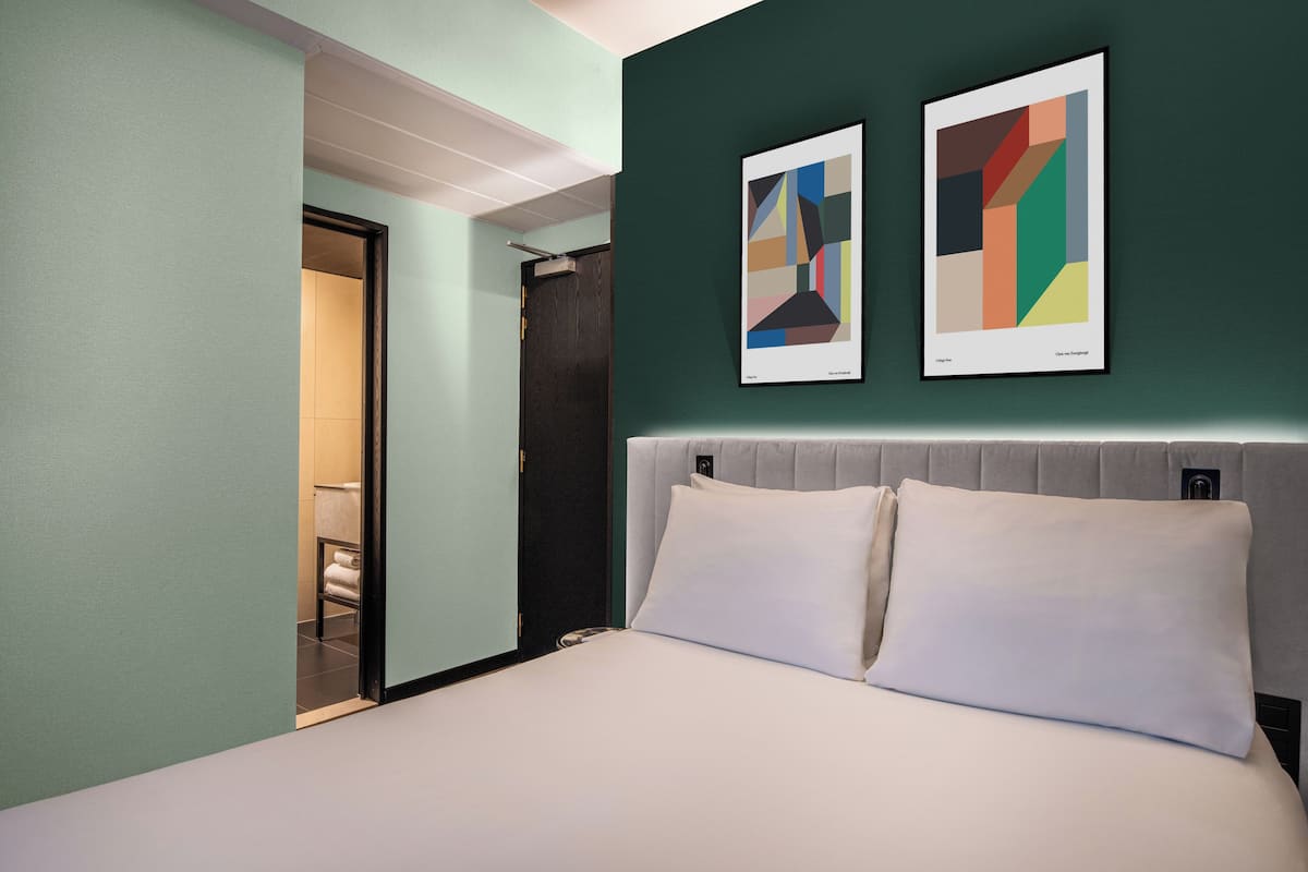 Una habitación de hotel con una cama, una puerta que da a un baño y dos obras de arte abstracto en la pared.