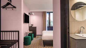 A hotel room with a bed, a desk, a chair, a small table, a mirror, and a window.