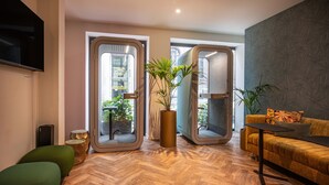 Una sala de estar moderna con un sofá, una mesa de centro y un televisor. Dos puertas dan a un balcón con plantas.