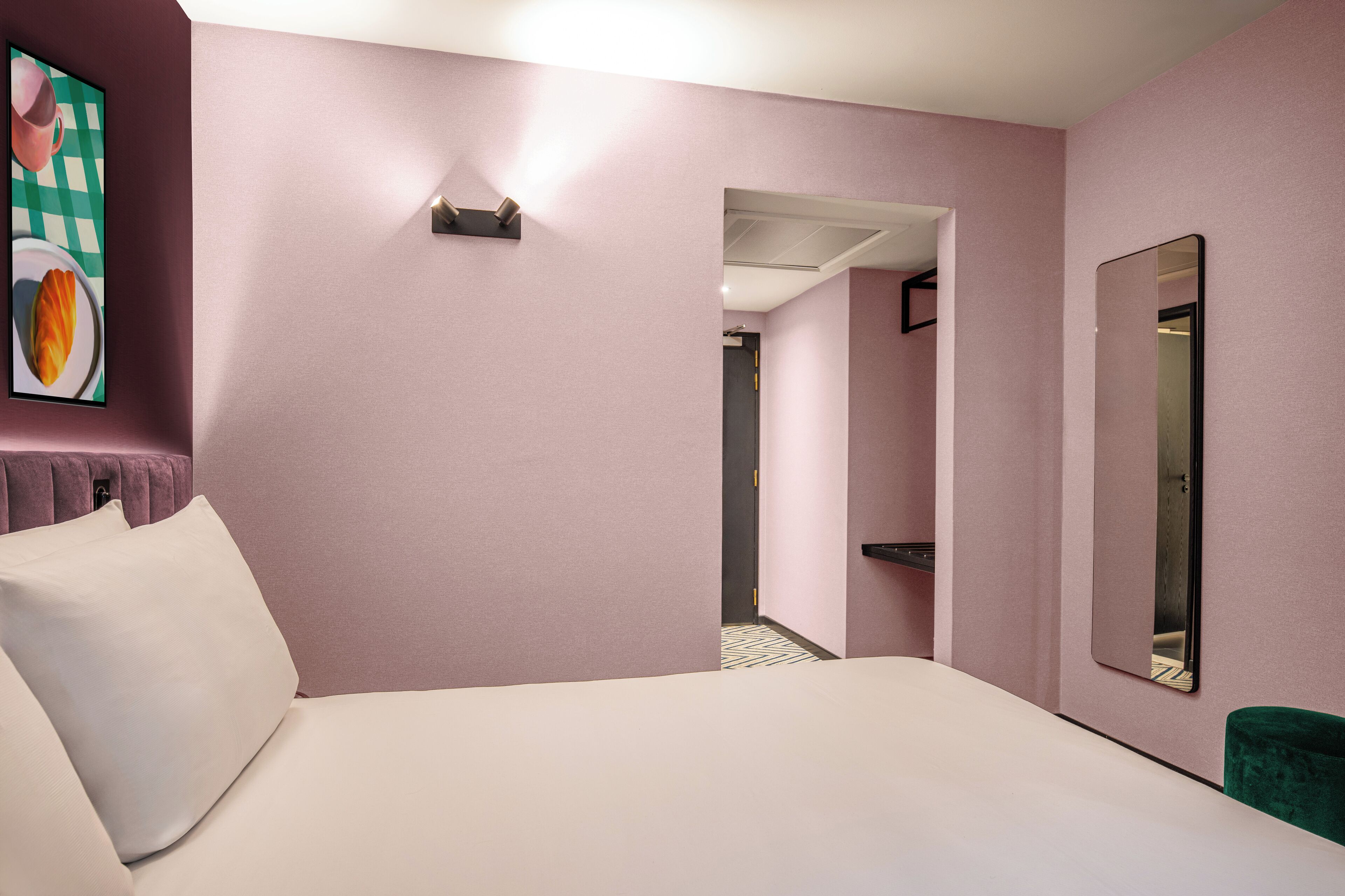 A hotel room with a bed, a large mirror, and a door leading to a hallway.