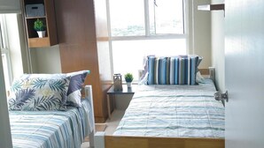 Un dormitorio con dos camas, una ventana, una estantería con cajas de almacenamiento y una mesita de noche con una planta.