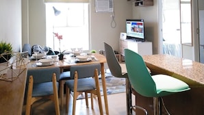 Una cocina moderna con comedor, que incluye una mesa de madera, sillas, un televisor y lámparas colgantes.