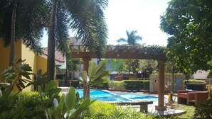 Un área de piscina con una pérgola, rodeada de abundante vegetación y palmeras.