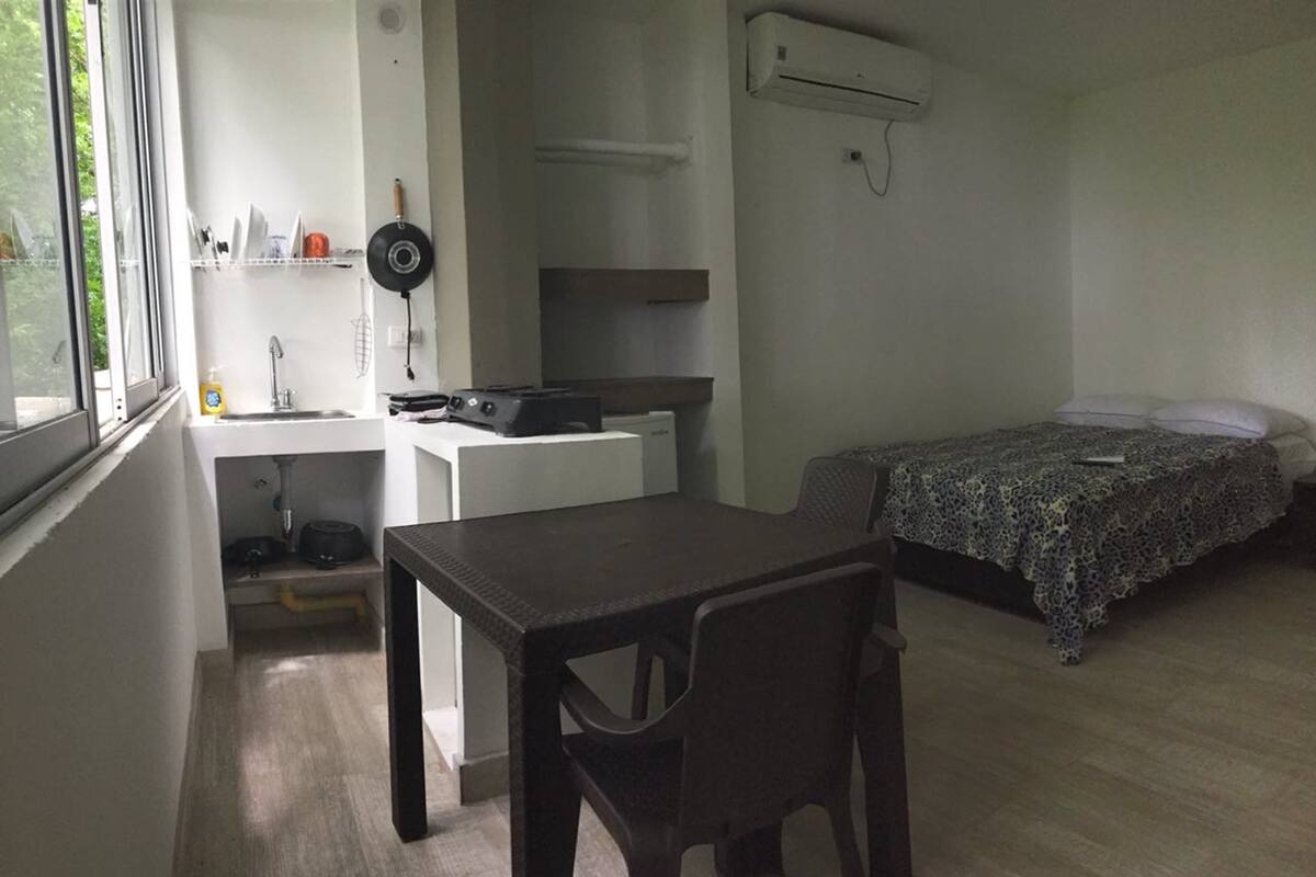 Une pièce de taille modeste comprenant un lit, un petit bureau avec une chaise, une fenêtre et un coin cuisine.